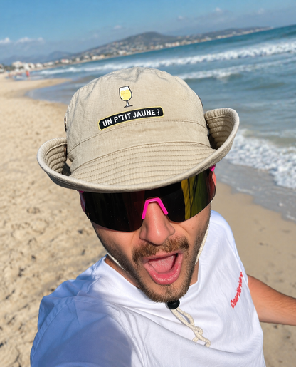 Bob à ficelle beige avec marqué un p'tit jaune porté par un homme à la plage 